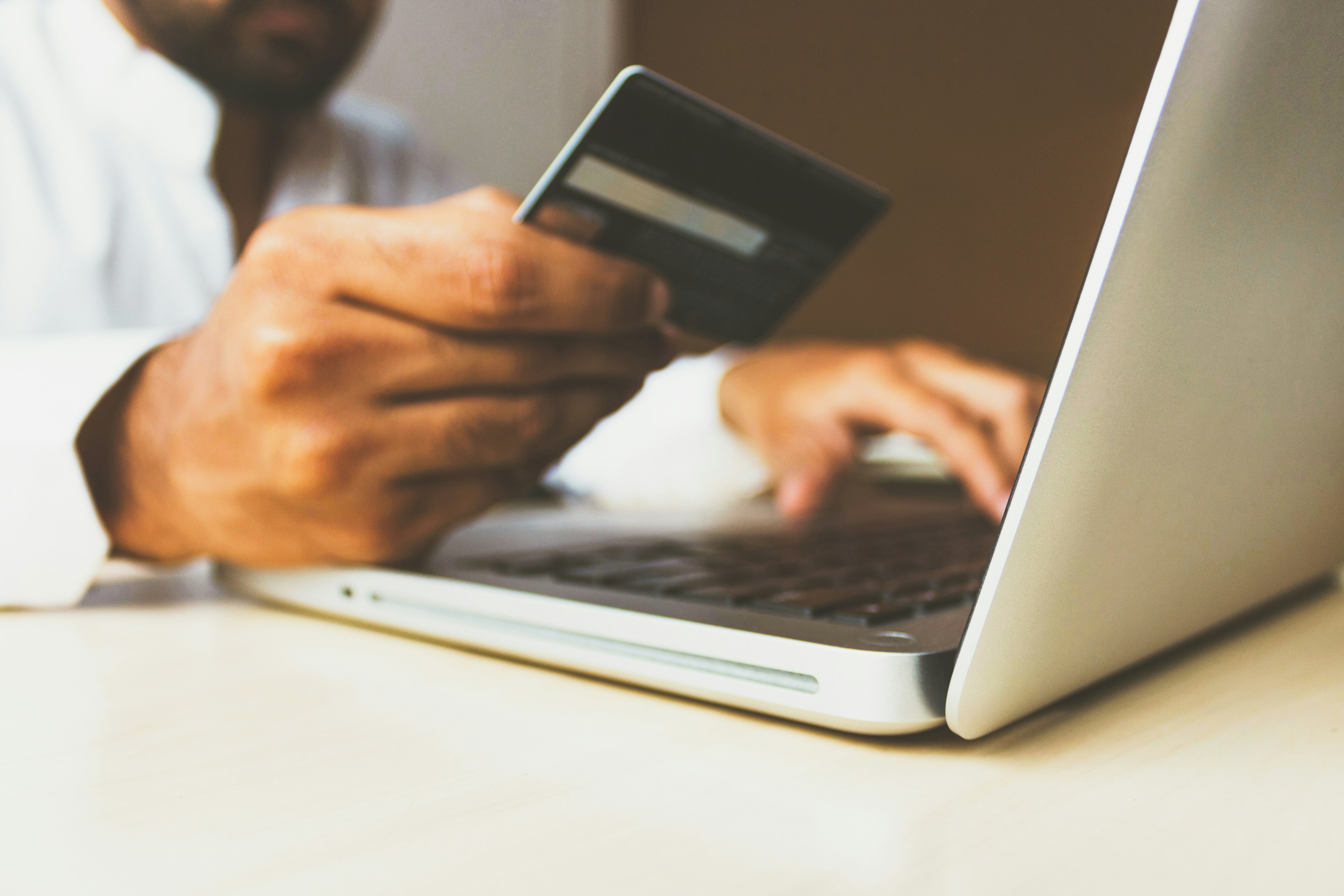 A person holding a credit card typing information on the laptop
